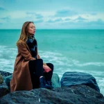 Joven en silencio sobre las rocas frente al mar en ivierno