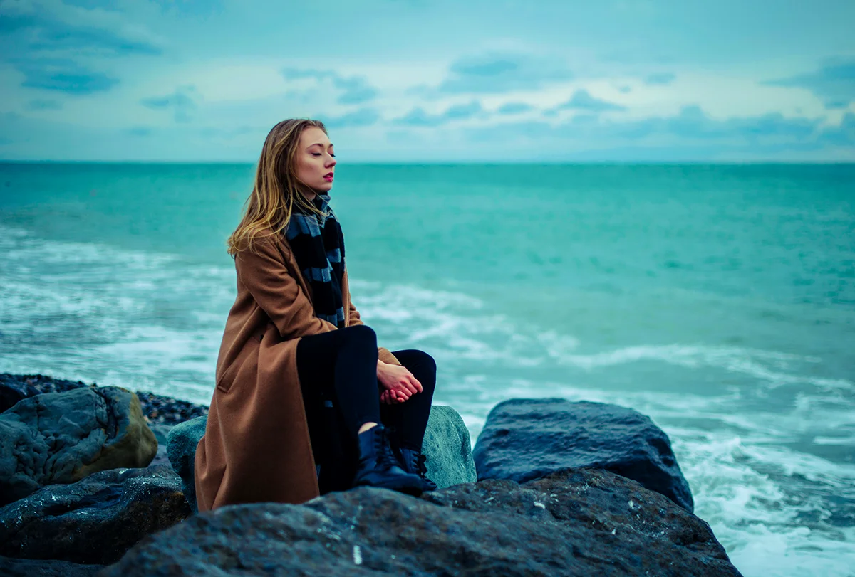 Joven en silencio sobre las rocas frente al mar en ivierno
